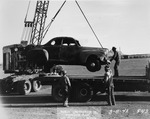 Photograph of men lifting a car onto the back of a truck