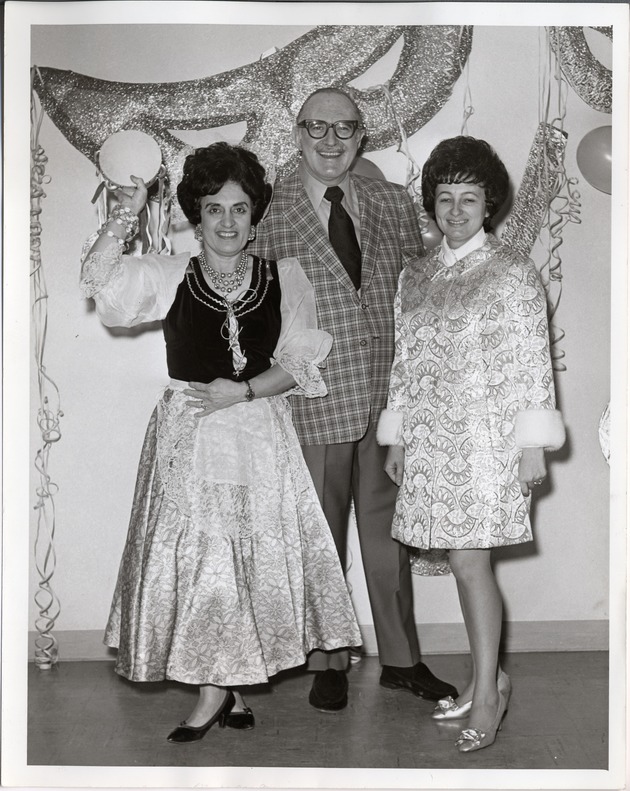 Photograph of Mrs. Lena Young, Mr. Forrest Duke, and Mrs. Buddy Sarkissian stand in front of Mardi Gras Ball decorations, Henderson, 1971