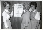 Photograph of Mrs. Phil Reinhardt, Mrs. J.S. Sobchik, and Mrs. Mary Gersich standing in front of a Mardi Gras Ball poster, Henderson, 1971