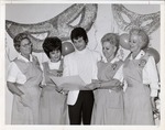 Photograph of four members of the Rose de Lima Hospital Auxiliary and a man standing in front of Mardi Gras Ball decorations, Henderson, 1971