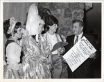 Photograph of three women dressed for the Mardi Gras Ball standing with a man holding a poster for the Ball, Henderson, 1969