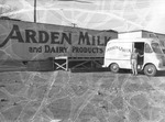 Photograph of a man standing by the Arden Milk and Dairy Products sign and truck, 1954